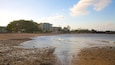 A beach with pebbles and waves, a building, and trees in the background.