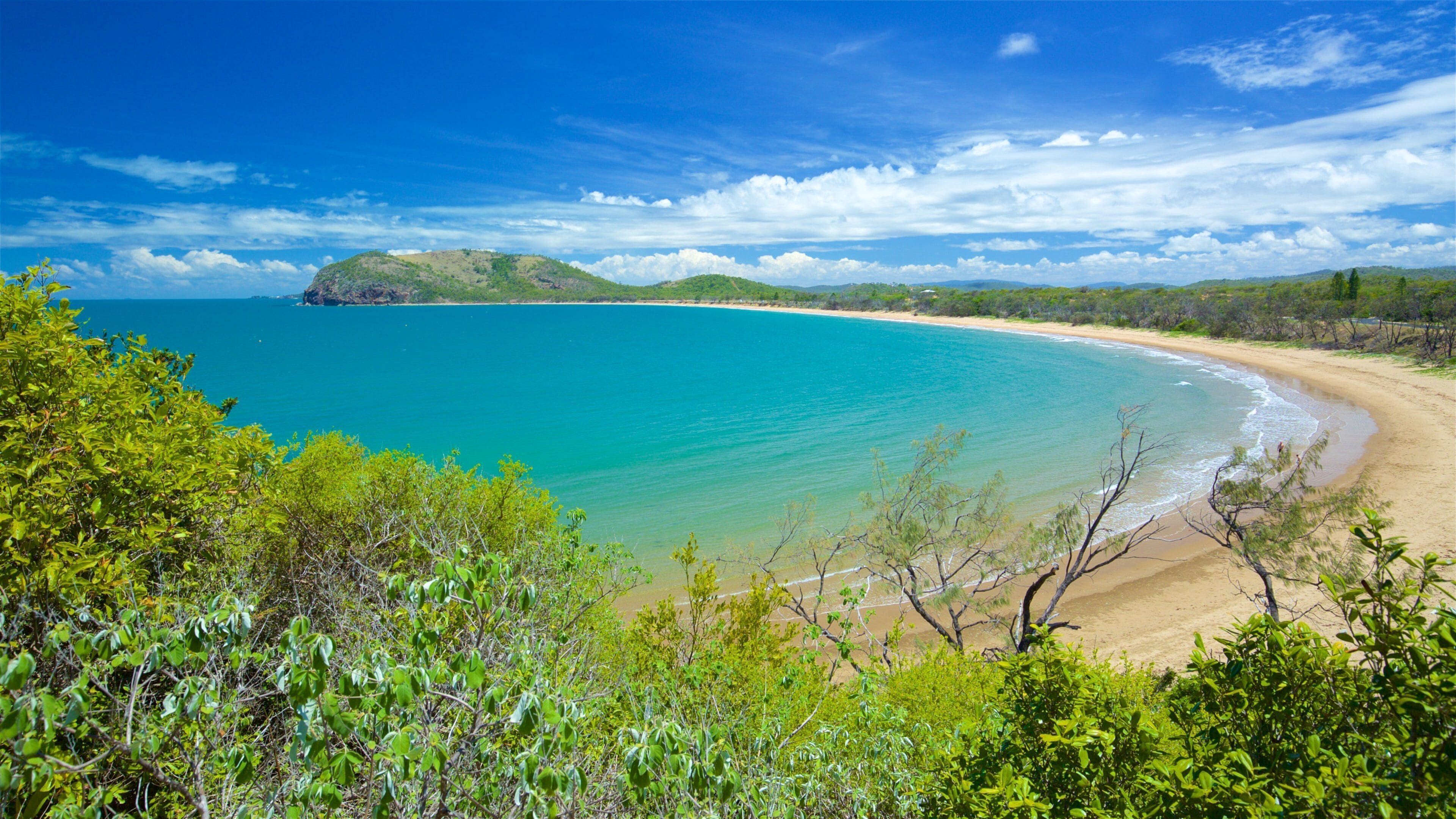 Paisagem costeira com mar turquesa, praia de areia e colinas verdes.