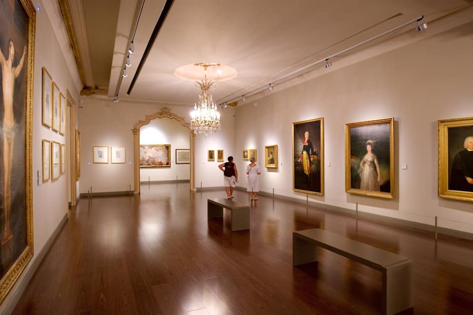 Een kunstgalerie met houten vloeren, schilderijen aan de wanden en een kroonluchter.