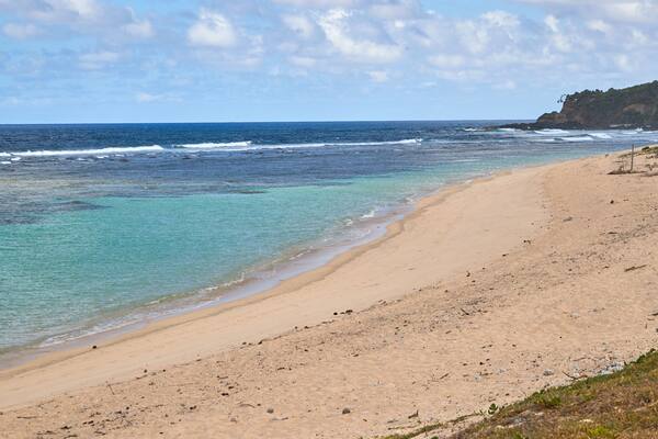 A beach with clear turquoise waters, a sandy shore, and a rocky cliff in the background.