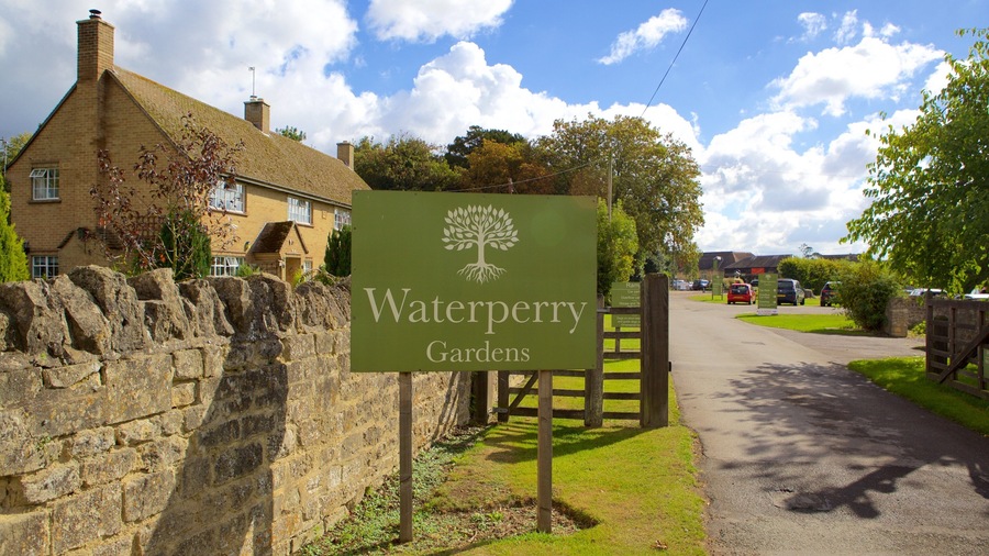 Letrero de los Jardines de Waterperry, con un muro de piedra y una casa al fondo.