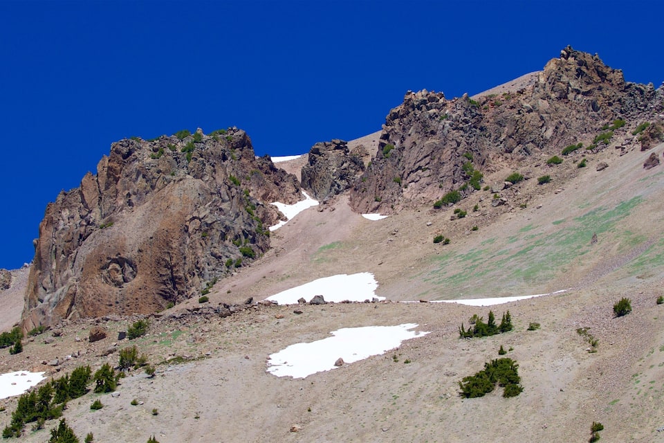 A rugged mountain landscape with rocky cliffs, patches of snow, and sparse vegetation.