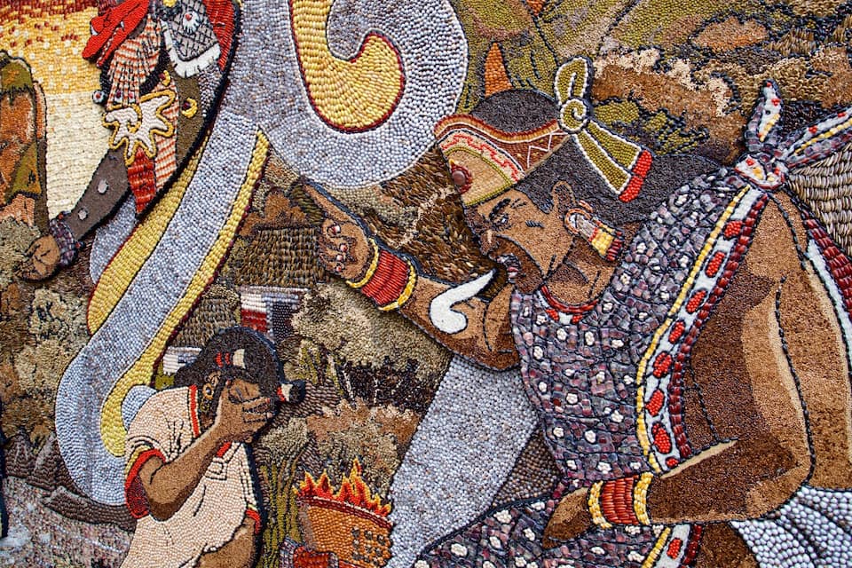 Une mosaïque détaillée, ornée de motifs et de figures complexes, comprenant un motif serpentin bien visible et une figure centrale parée de bijoux élaborés.