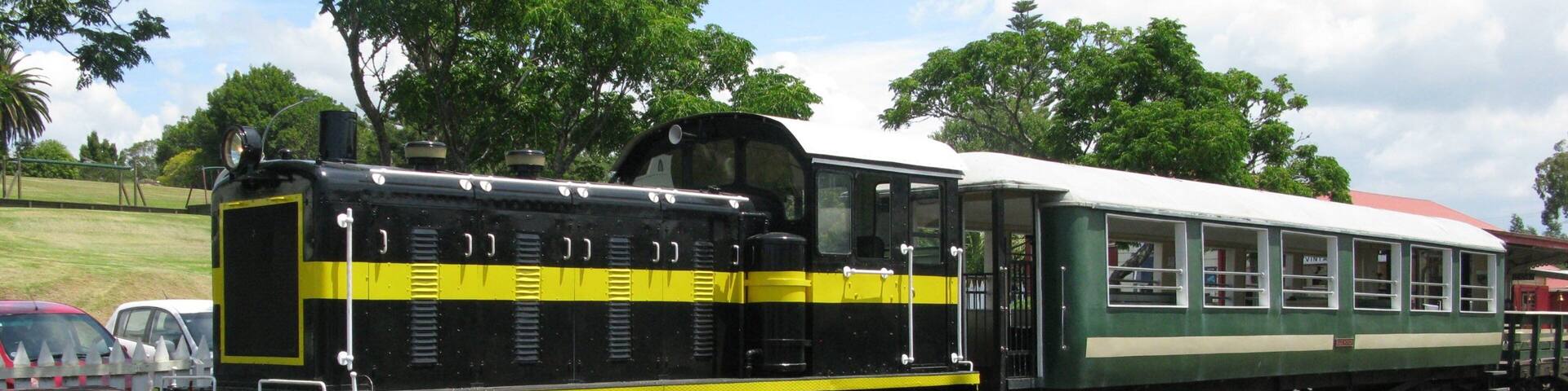 Un tren antiguo con locomotora negra y amarilla y vagones de pasajeros verdes estacionado sobre rieles.