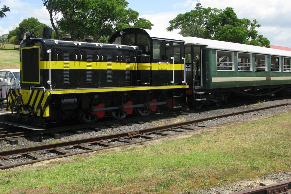 Un train d’époque, avec une locomotive noire et jaune et des wagons de voyageurs verts, est garé sur les voies.