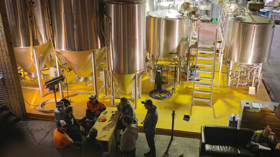 Uma cervejaria com tanques de aço inoxidável e chão amarelo.