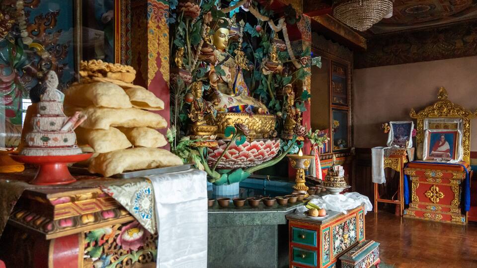 A richly decorated temple interior with a large Buddha statue, ornate decorations, and traditional offerings.