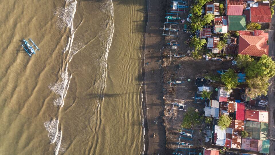 An aerial view of a coastal village with boats, houses, and a beach.
