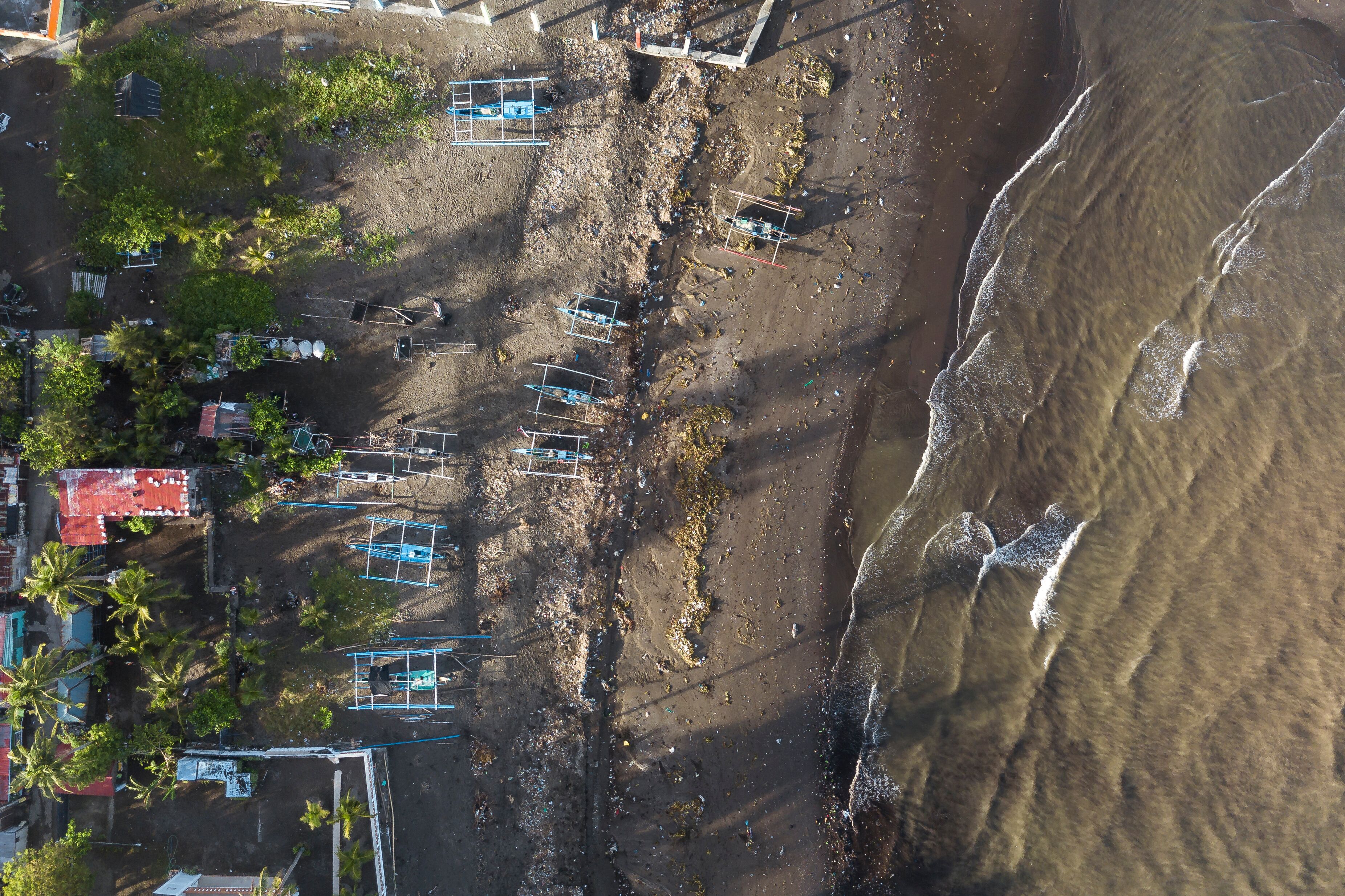 Top view of the coastline of Naic, Cavite, Philippines. A polluted beachfront visibly littered with trash. Traditional fishing boats parked at the beach.