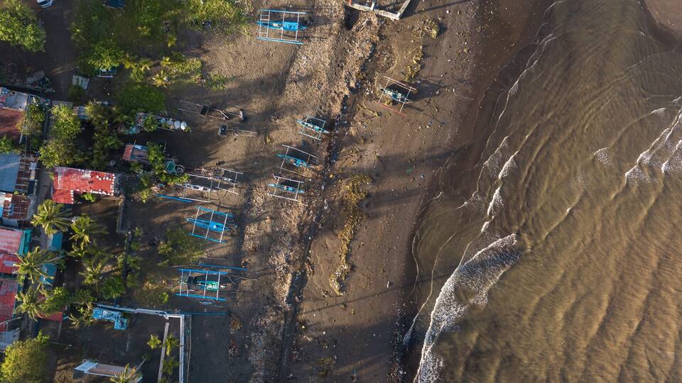 An aerial view of a beach with boats, palm trees, and buildings.