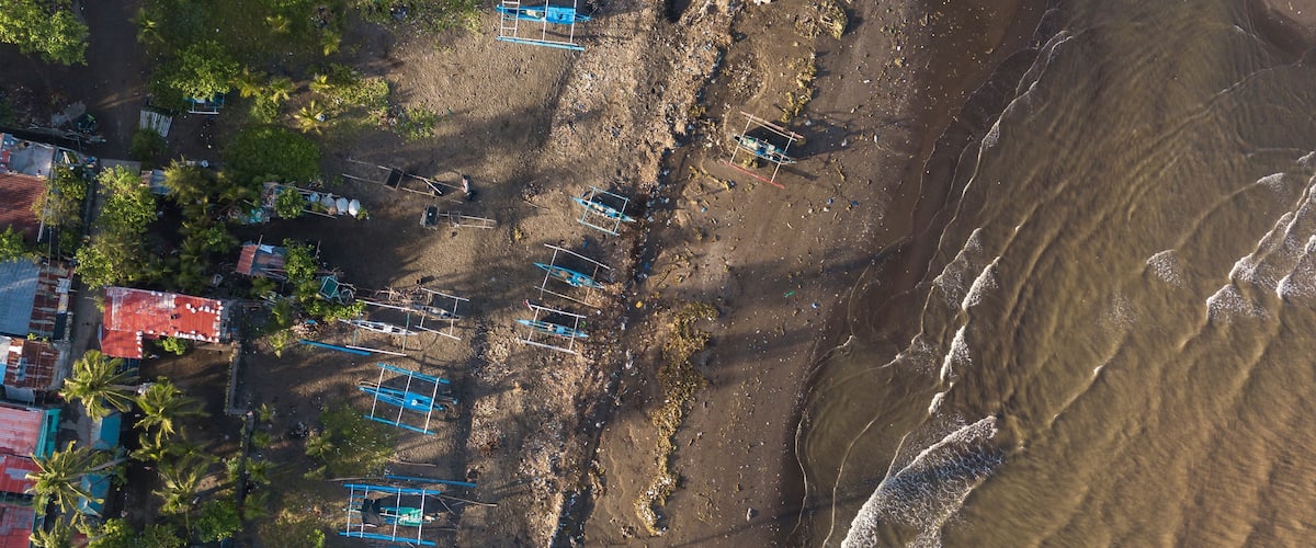 An aerial view of a beach with boats, palm trees, and buildings.
