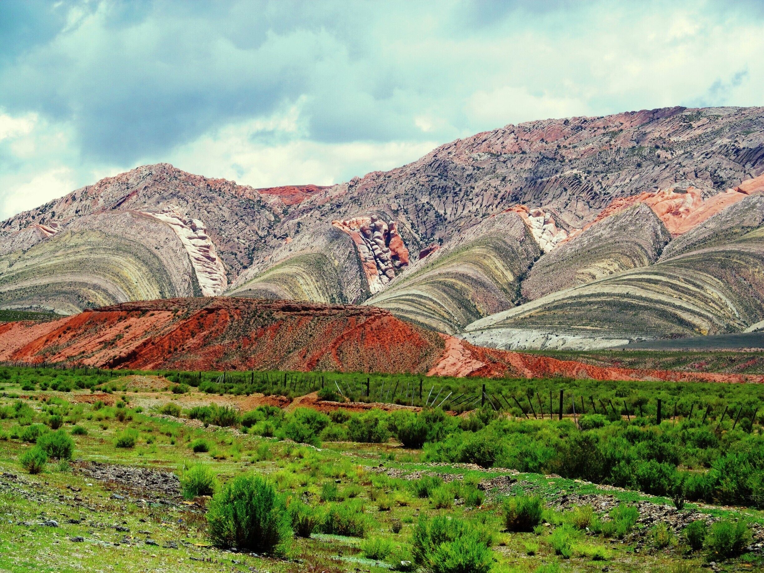 A mountainous landscape with layered rock formations and green vegetation in the foreground.
