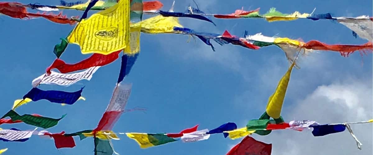 Prayer flags strung across a mountain range with a snow-capped peak in the background.