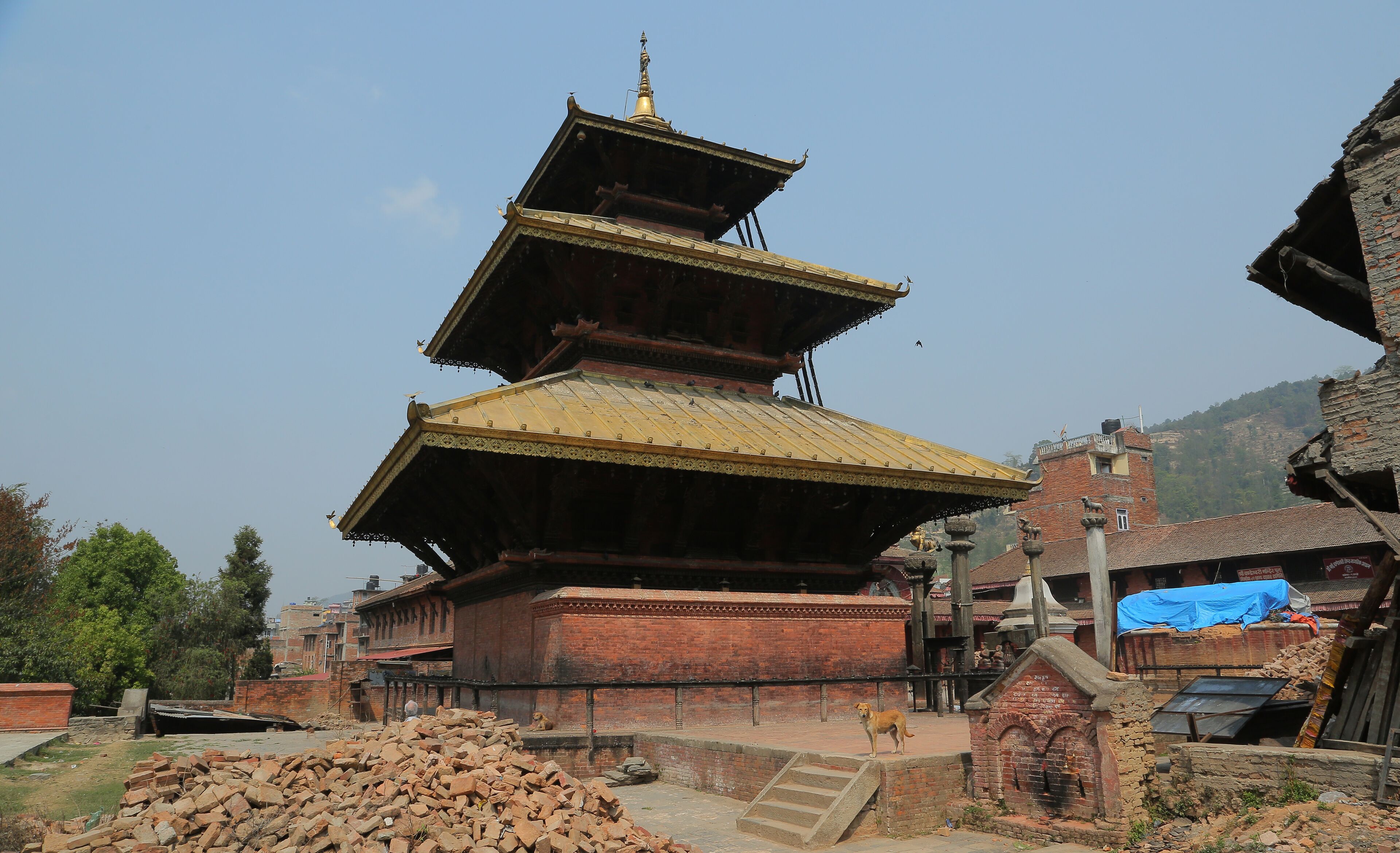 A traditional multi-tiered pagoda with a golden roof, surrounded by brick buildings and a pile of bricks.