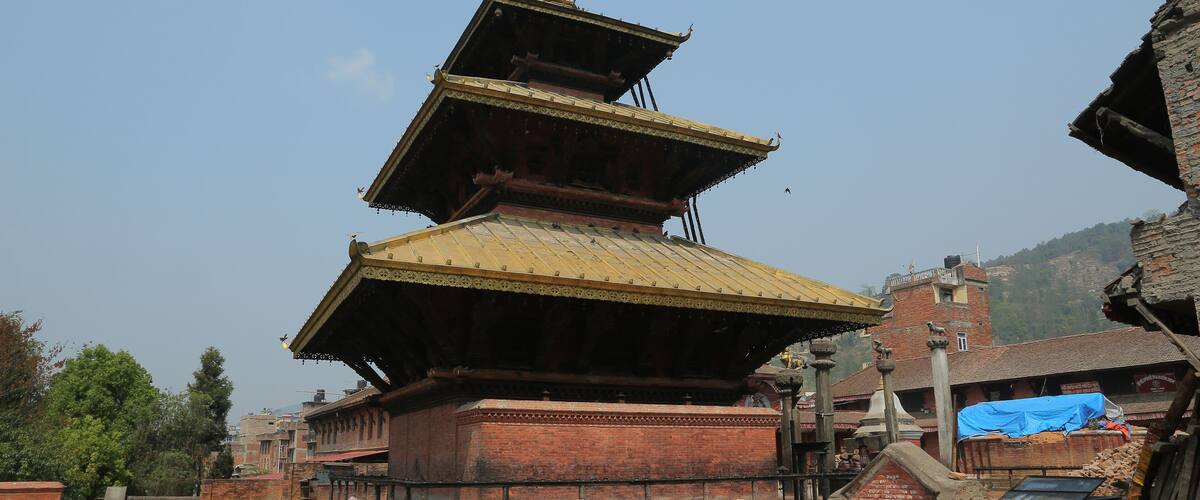 A traditional multi-tiered pagoda with a golden roof, surrounded by brick buildings and a pile of bricks.