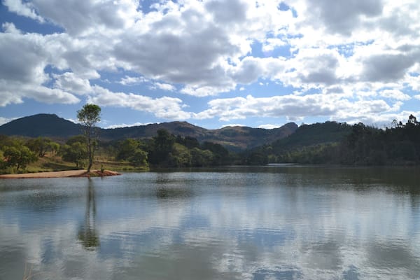 A calm lake surrounded by hills and trees under a partly cloudy sky.