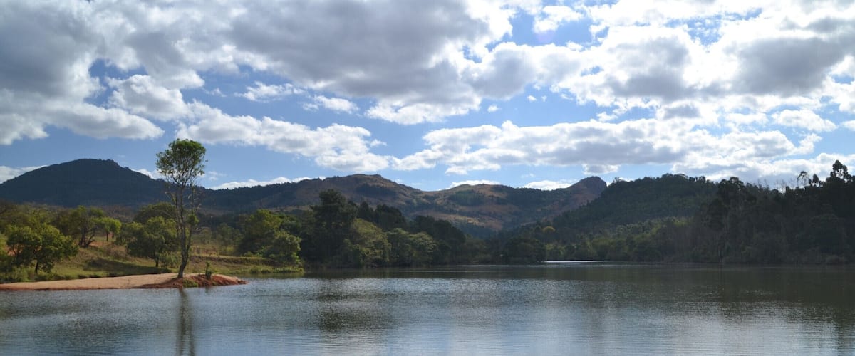 A calm lake surrounded by hills and trees under a partly cloudy sky.