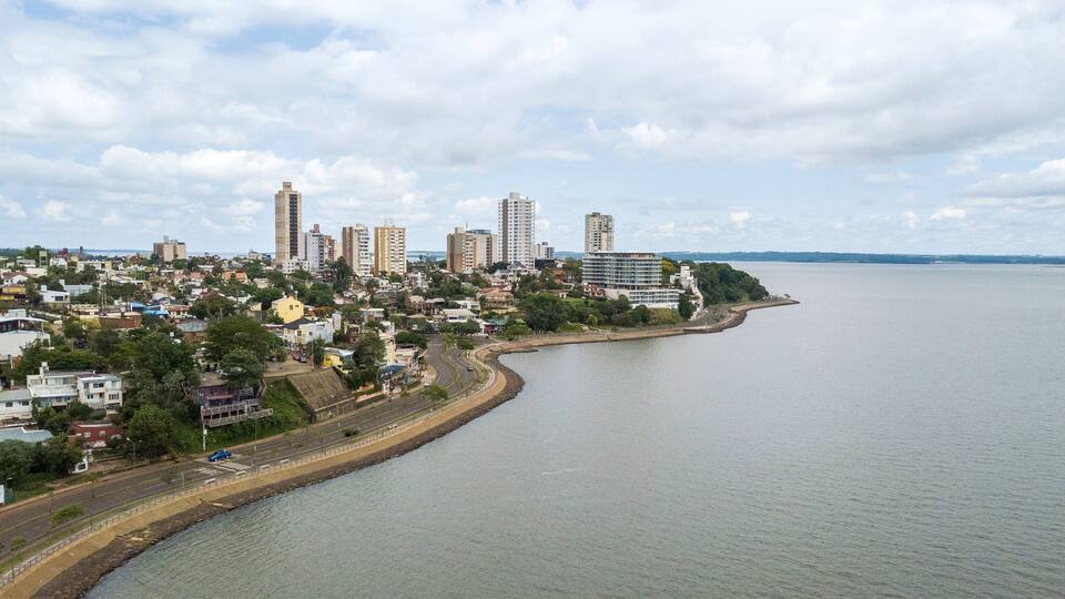 A coastal cityscape with a curved road along the waterfront, high-rise buildings, and a clear sky.