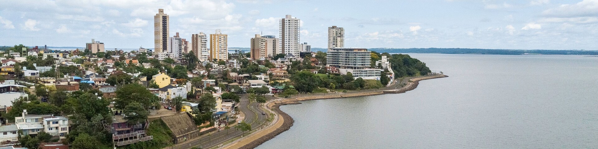 Un paisaje urbano costero con una carretera curva a lo largo del frente marítimo, edificios altos y un cielo despejado.