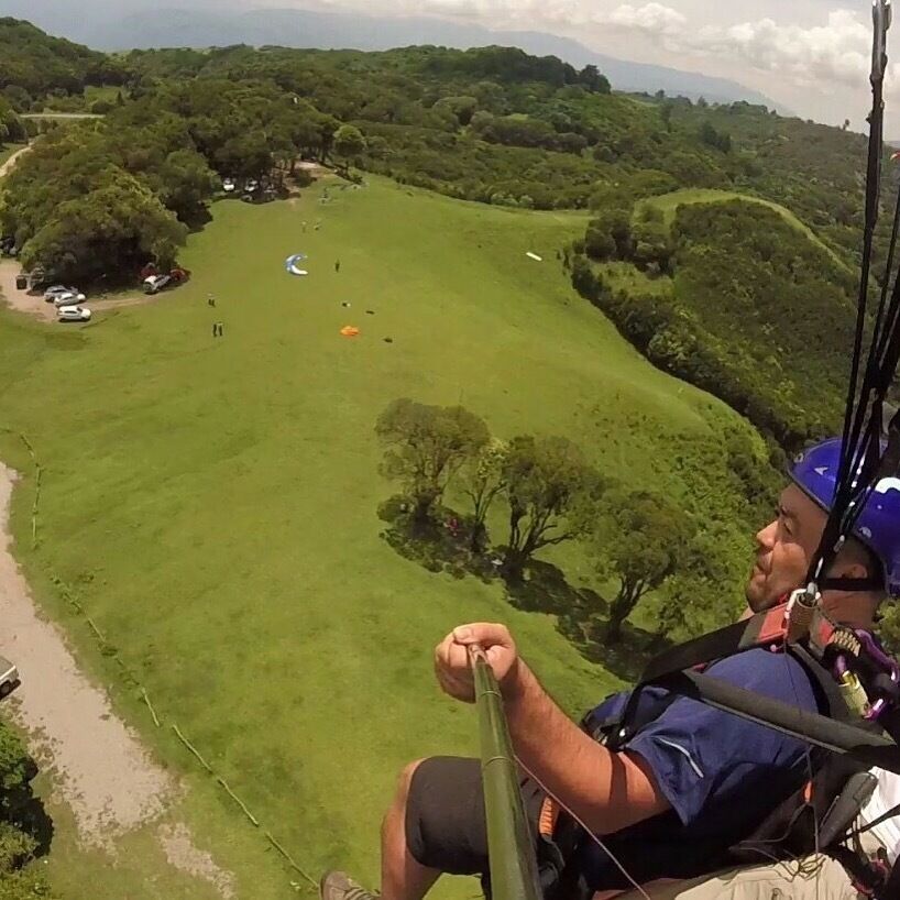 A person in a blue shirt and helmet preparing to rappel down a grassy hillside.