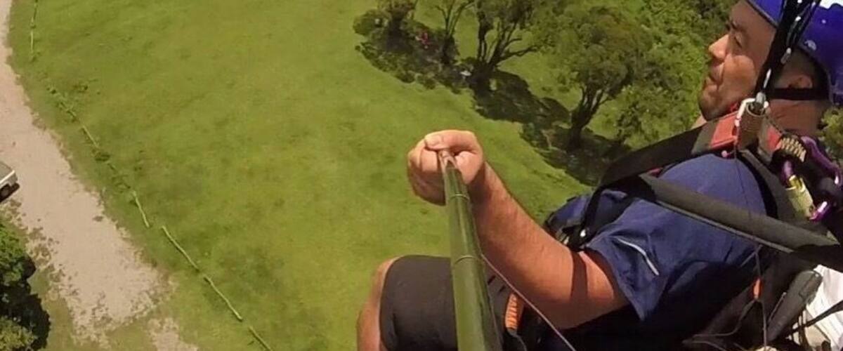 A person in a blue shirt and helmet preparing to rappel down a grassy hillside.
