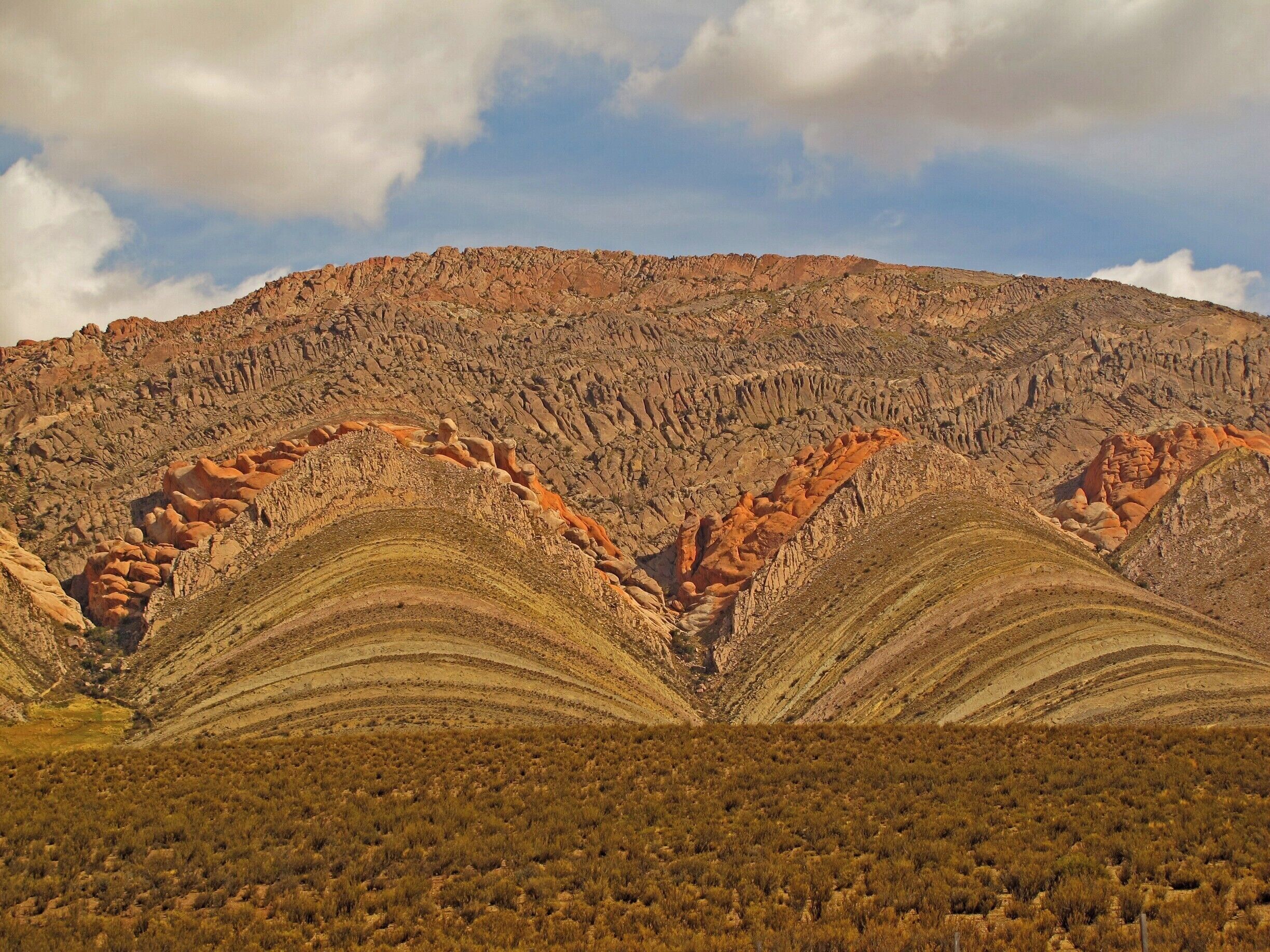 A rugged mountain landscape with layered rock formations and sparse vegetation.