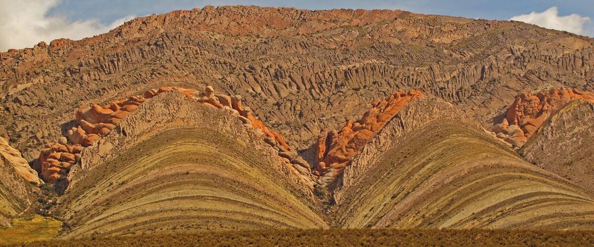 A rugged mountain landscape with layered rock formations and sparse vegetation.