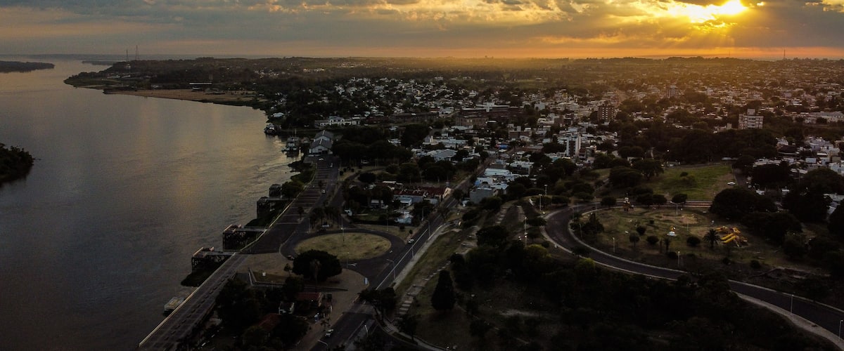 Un atardecer sobre una ciudad costera con un río, carreteras y zonas residenciales.