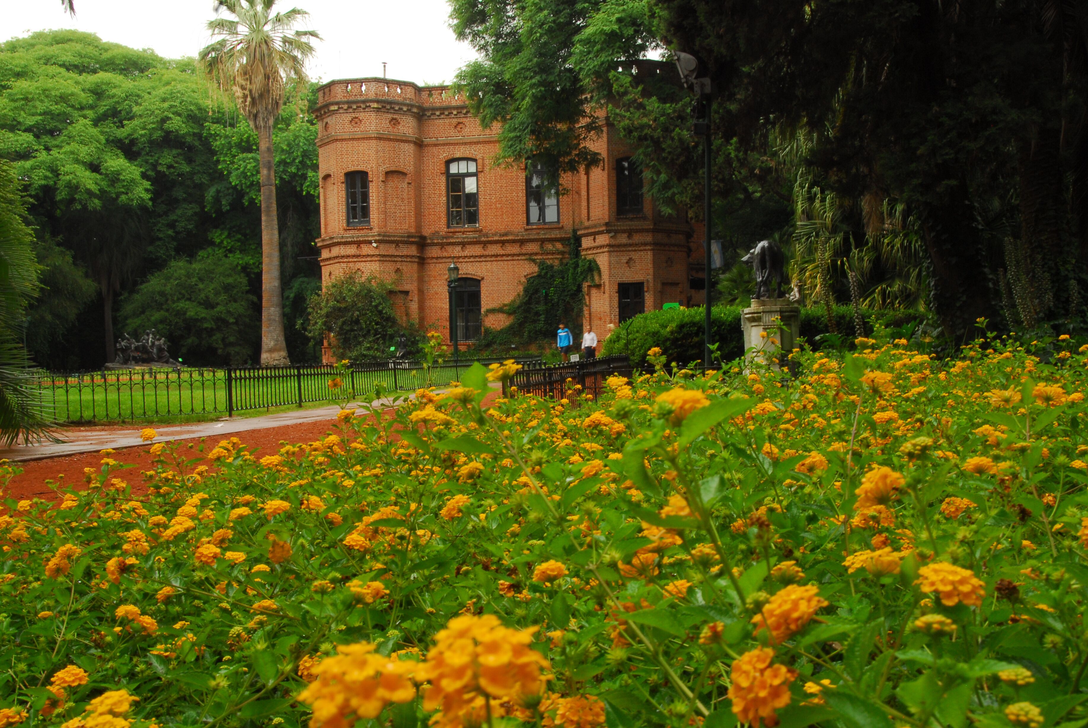 A brick building surrounded by lush greenery and a field of yellow flowers.