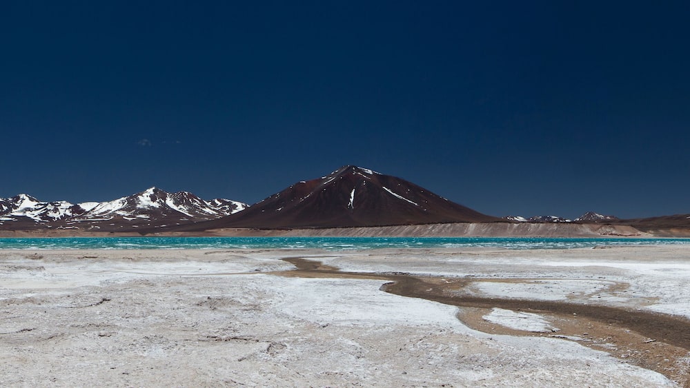 Volcanic landscape in the Andes mountain range. Panorama view of the turquoise color water lake called Green Lagoon, the dark mountains with snowy peaks and volcanoes, high in the cordillera.