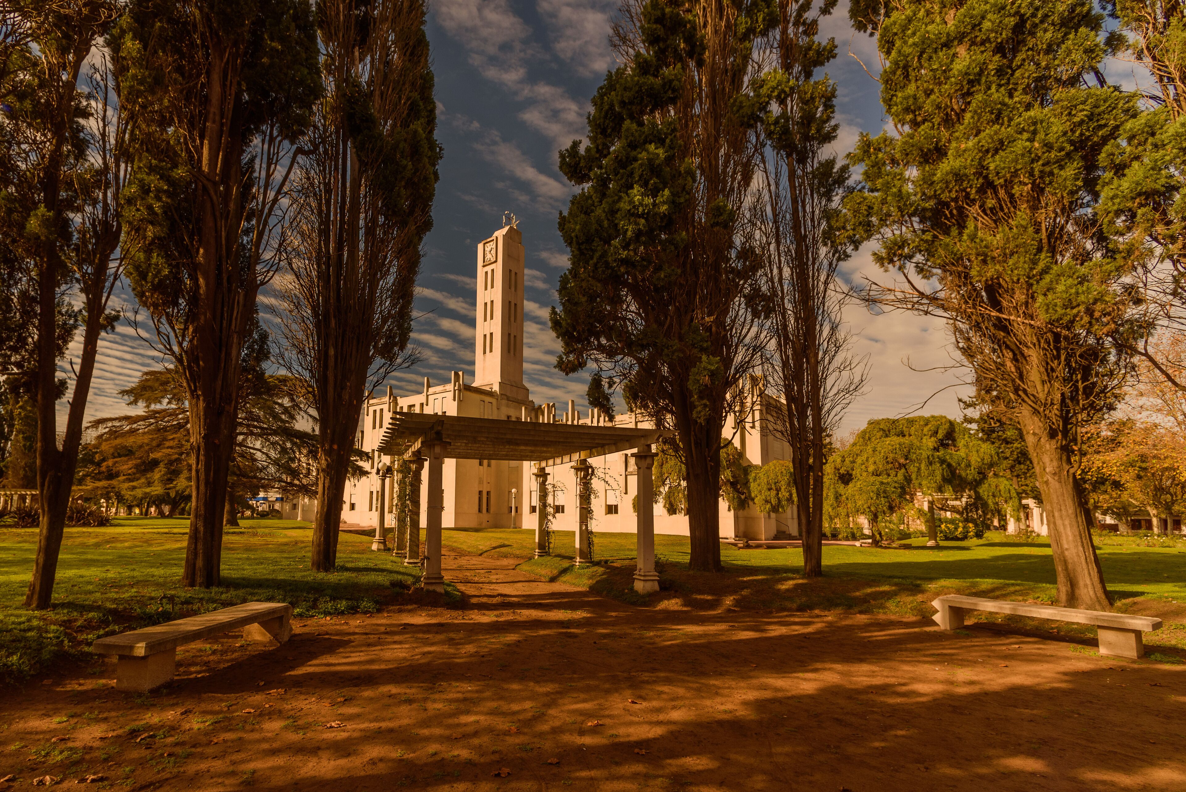 A park with a gazebo, trees, and a building with a clock tower.
