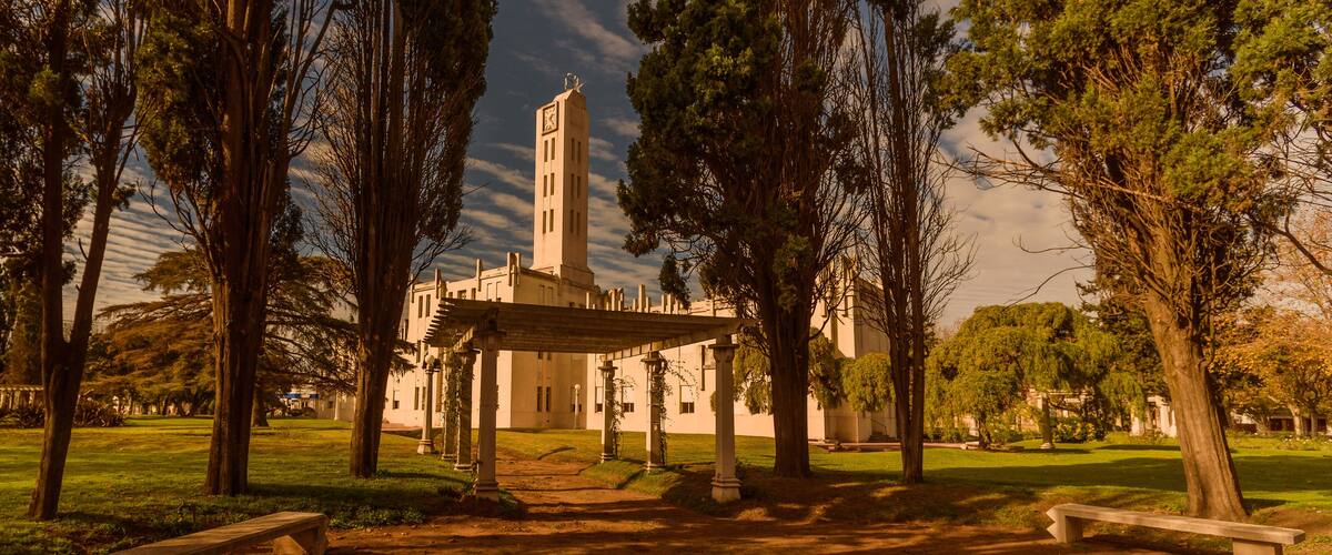 A park with a gazebo, trees, and a building with a clock tower.