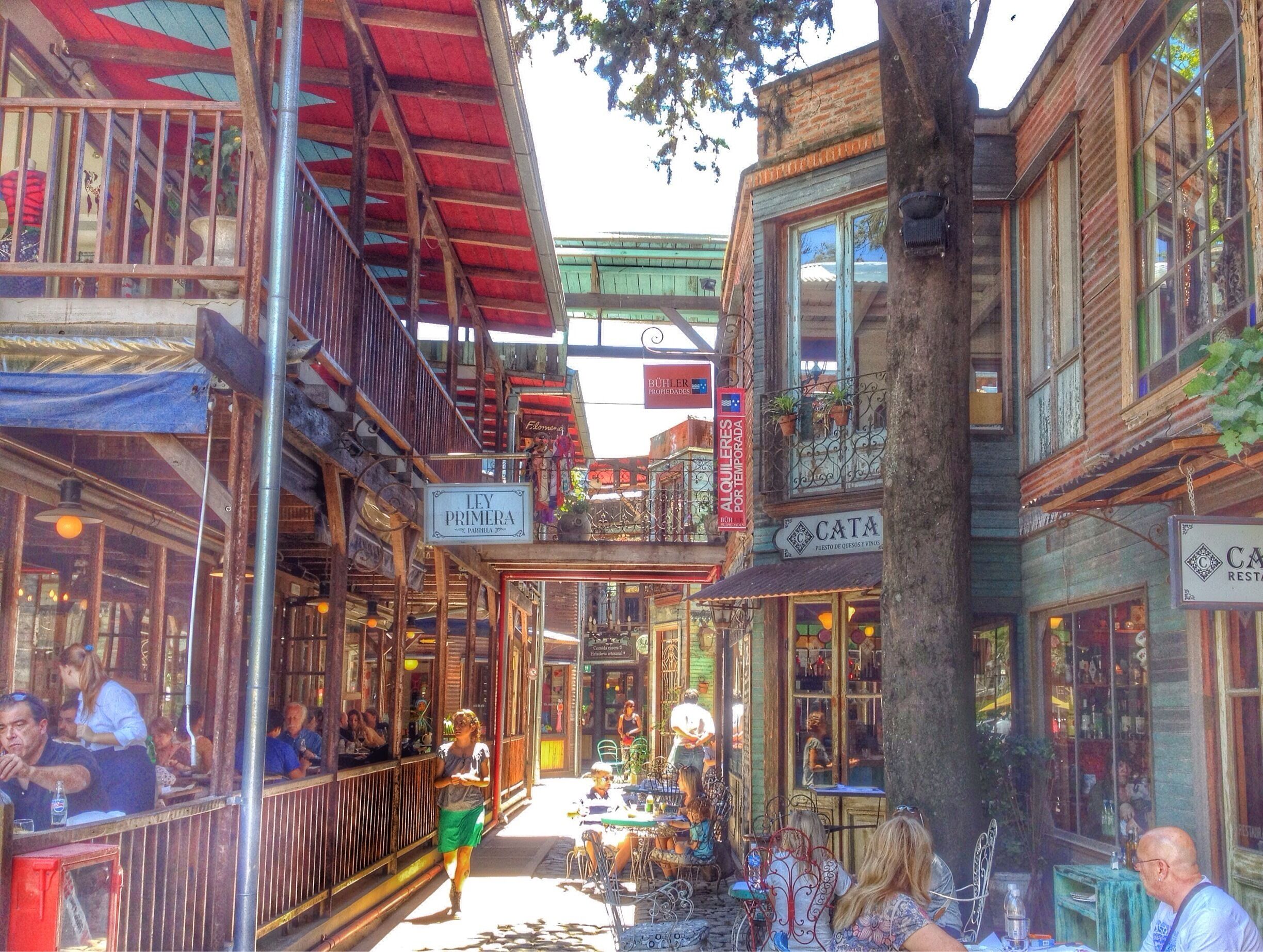 A bustling street with wooden buildings, outdoor seating, and various shops.