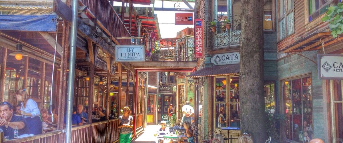 A bustling street with wooden buildings, outdoor seating, and various shops.