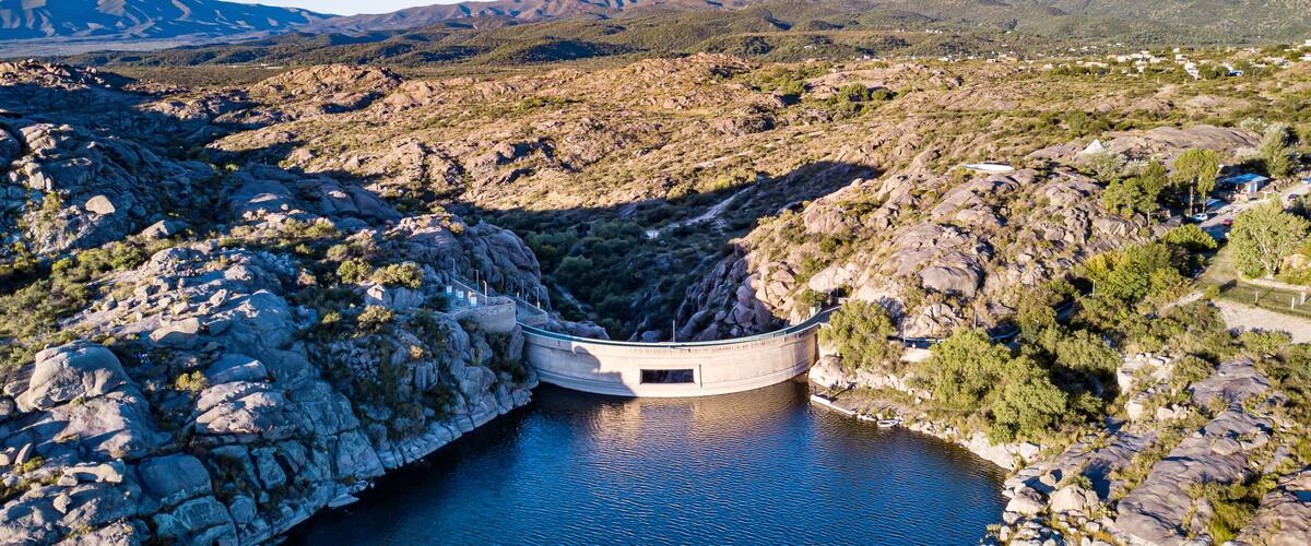 A dam with a reservoir, surrounded by rocky terrain and mountains.