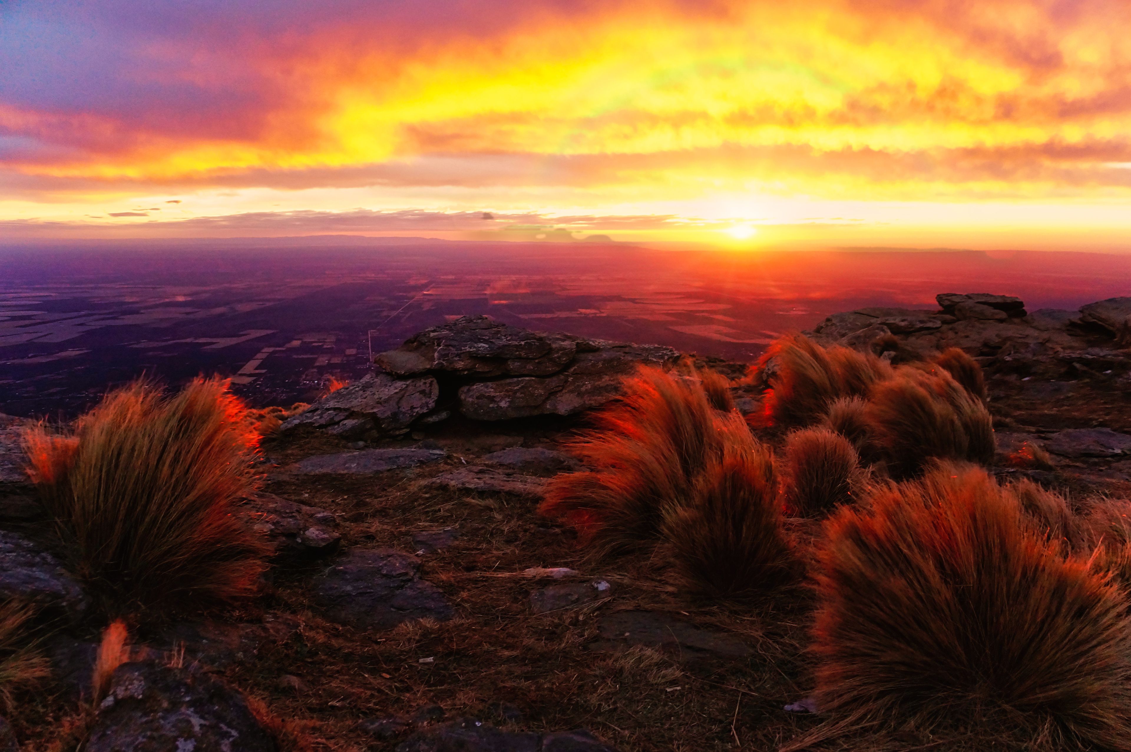 Ein Sonnenuntergang über einer gebirgigen Landschaft mit Felsformationen und trockenem Gras.