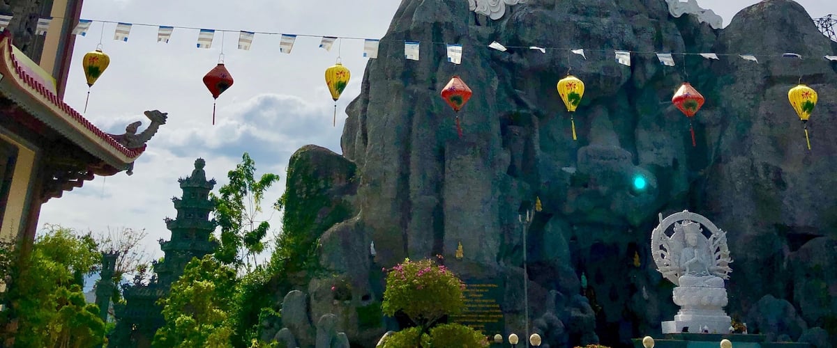 Eine große weiße Statue auf einem Felsen, im Hintergrund eine Pagode.