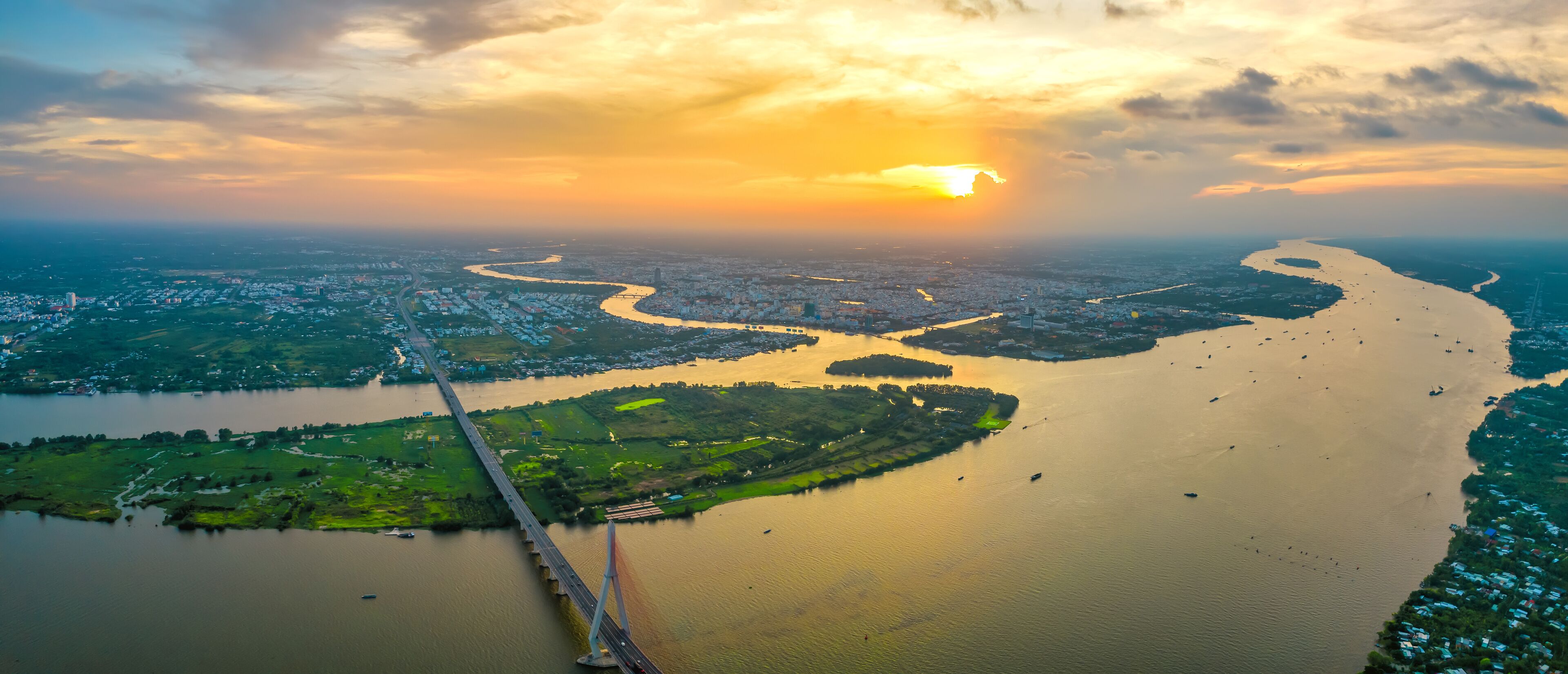 A river winding through a city, a bridge crossing the river, and a sunset in the background.