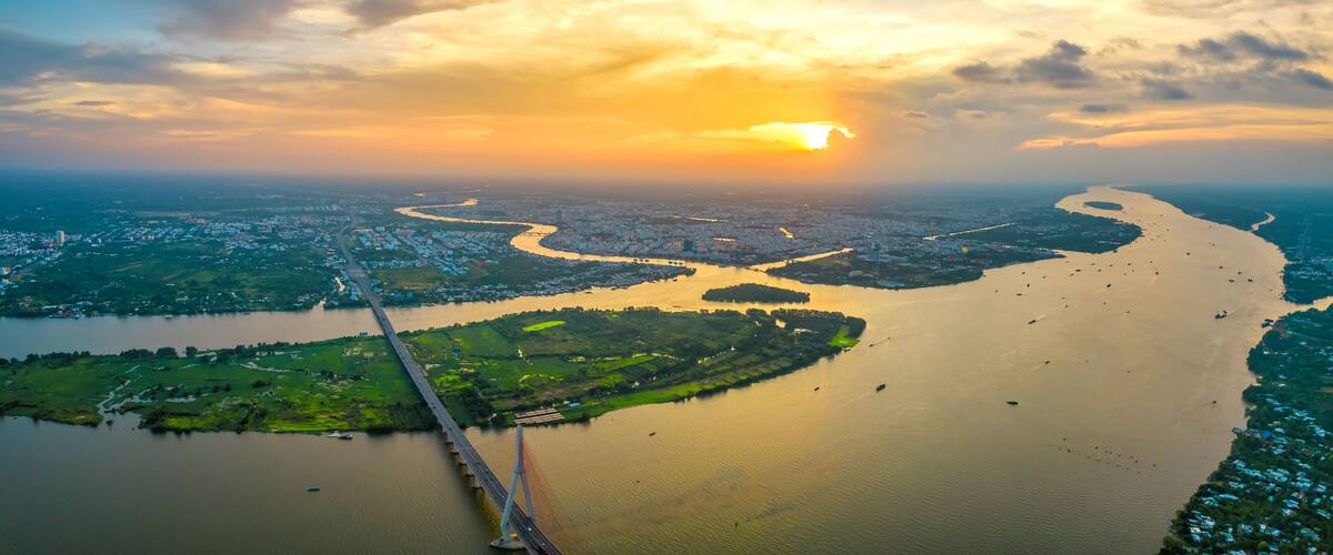 A river winding through a city, a bridge crossing the river, and a sunset in the background.