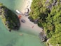 Vista aérea de una playa con un bote, kayaks y una tabla de remo roja.