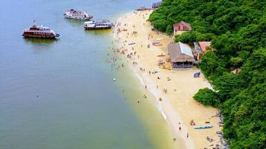 A beach with boats, a sandy shore, and lush green hills.