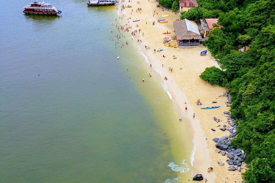 Uma praia com barcos, areal arenoso e colinas verdes exuberantes.