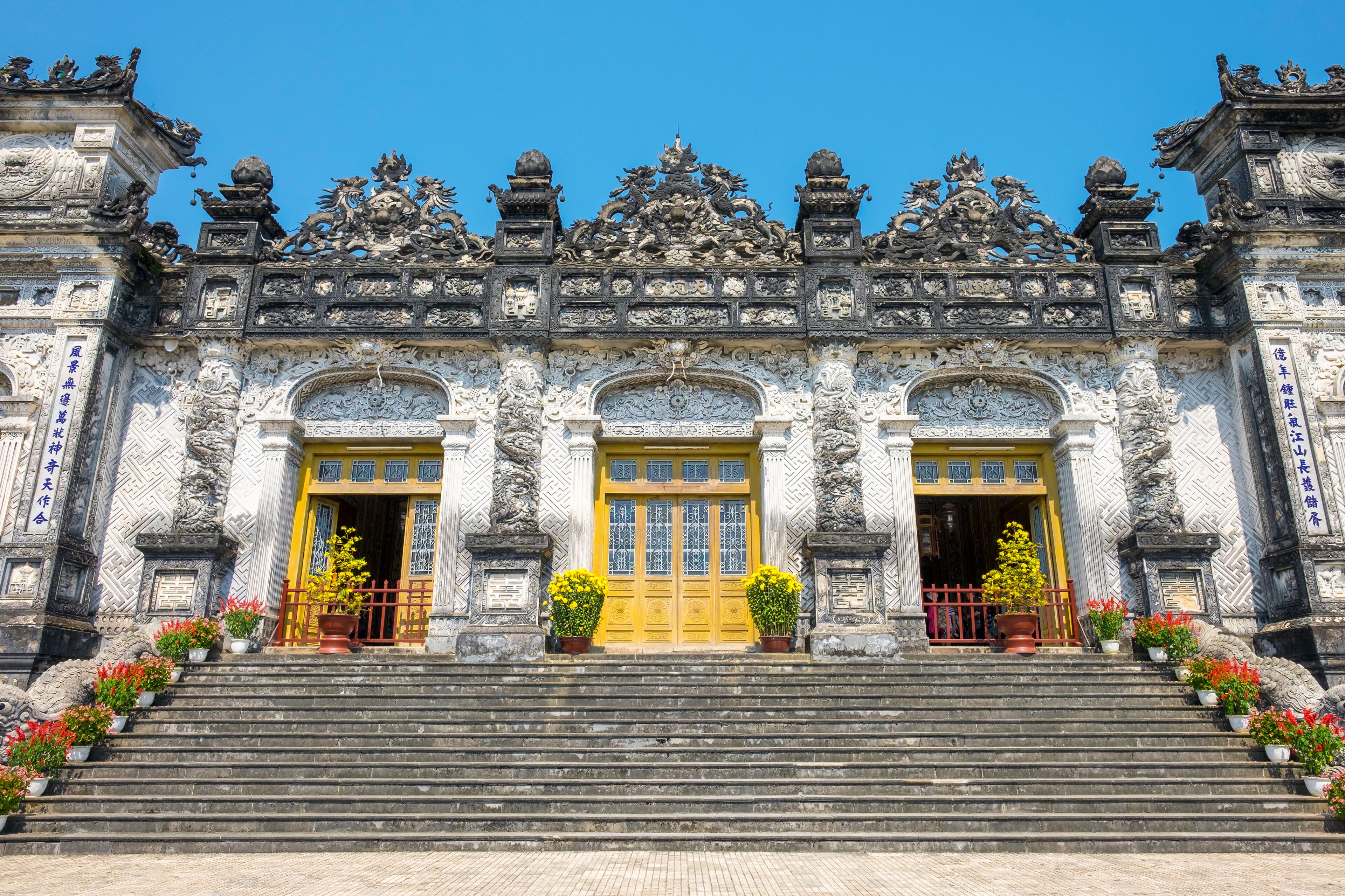 A grand temple with ornate carvings, a yellow central door, and steps adorned with flowers.