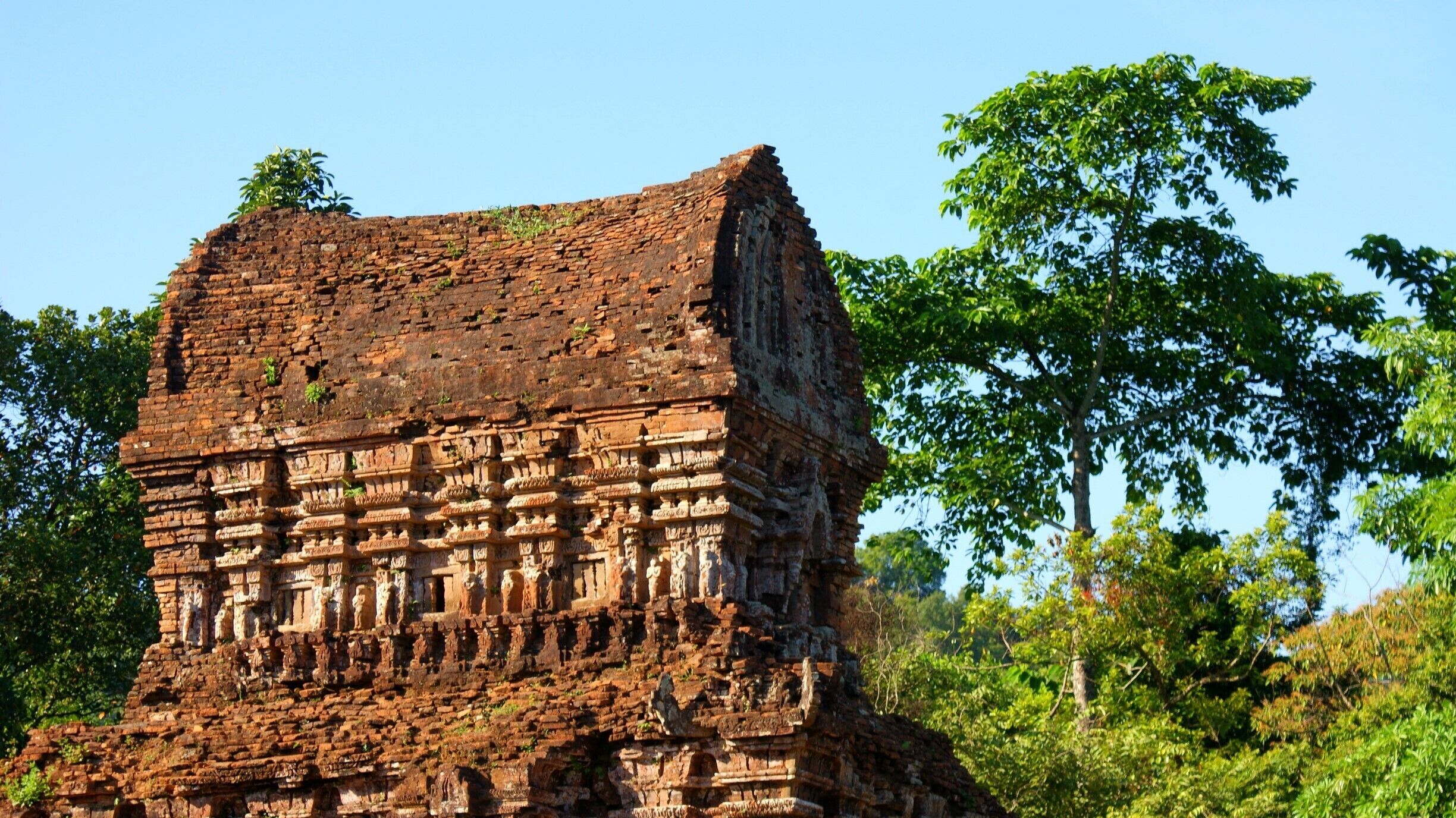 An ancient brick structure with intricate carvings, surrounded by lush greenery.