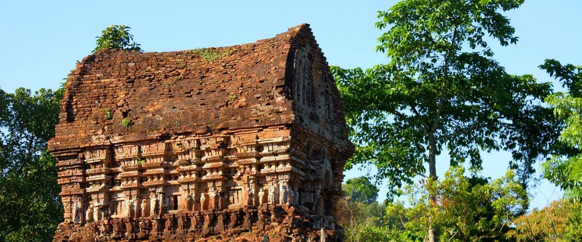 An ancient brick structure with intricate carvings, surrounded by lush greenery.