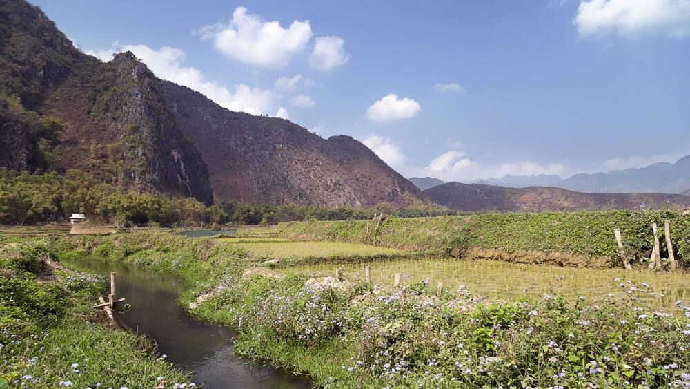 Ein Fluss fließt durch ein Tal, im Hintergrund Berge und ein kleines Haus in der Nähe des Wassers.