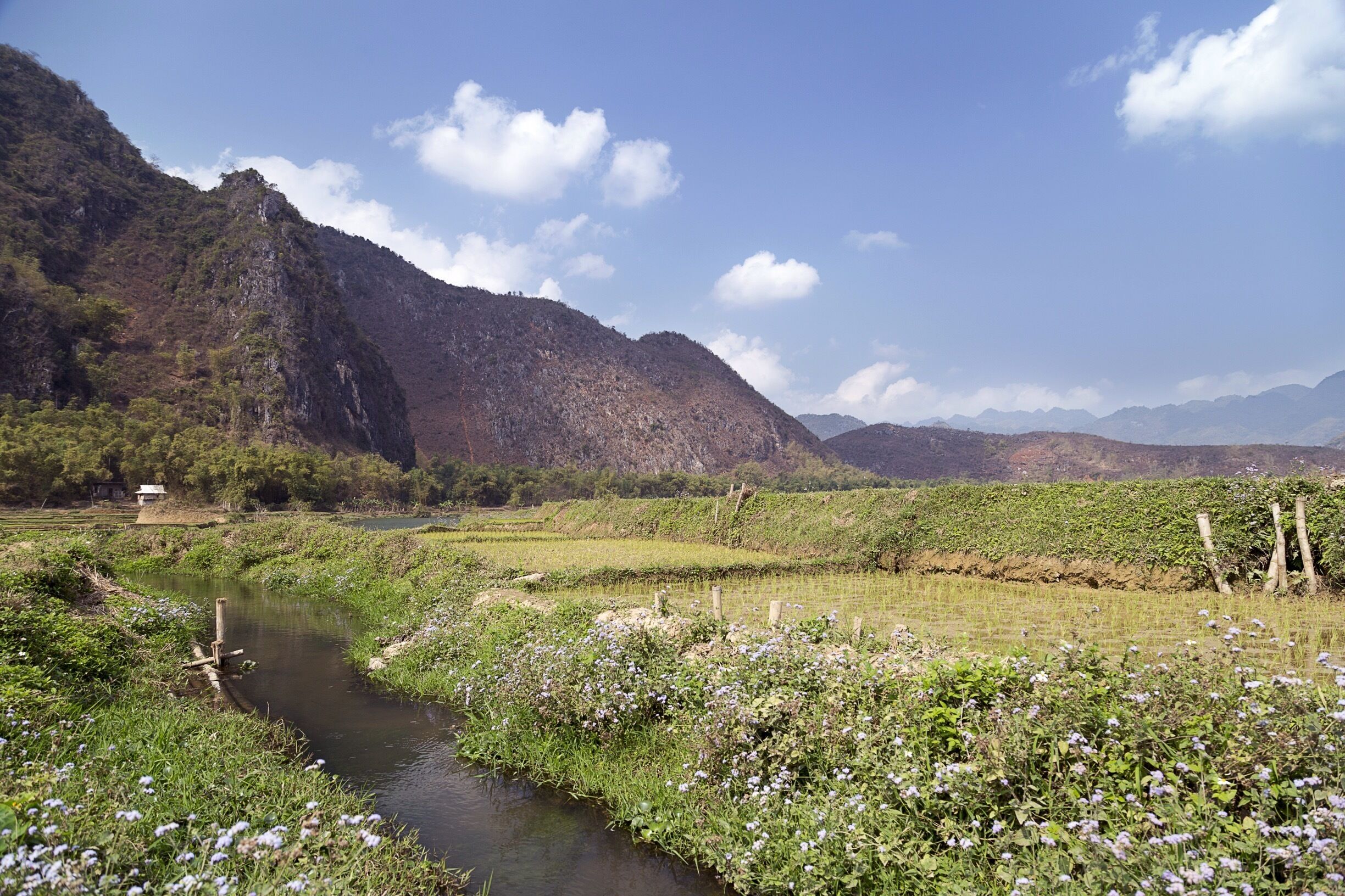 A river flowing through a valley with mountains in the background and a small house near the water.
