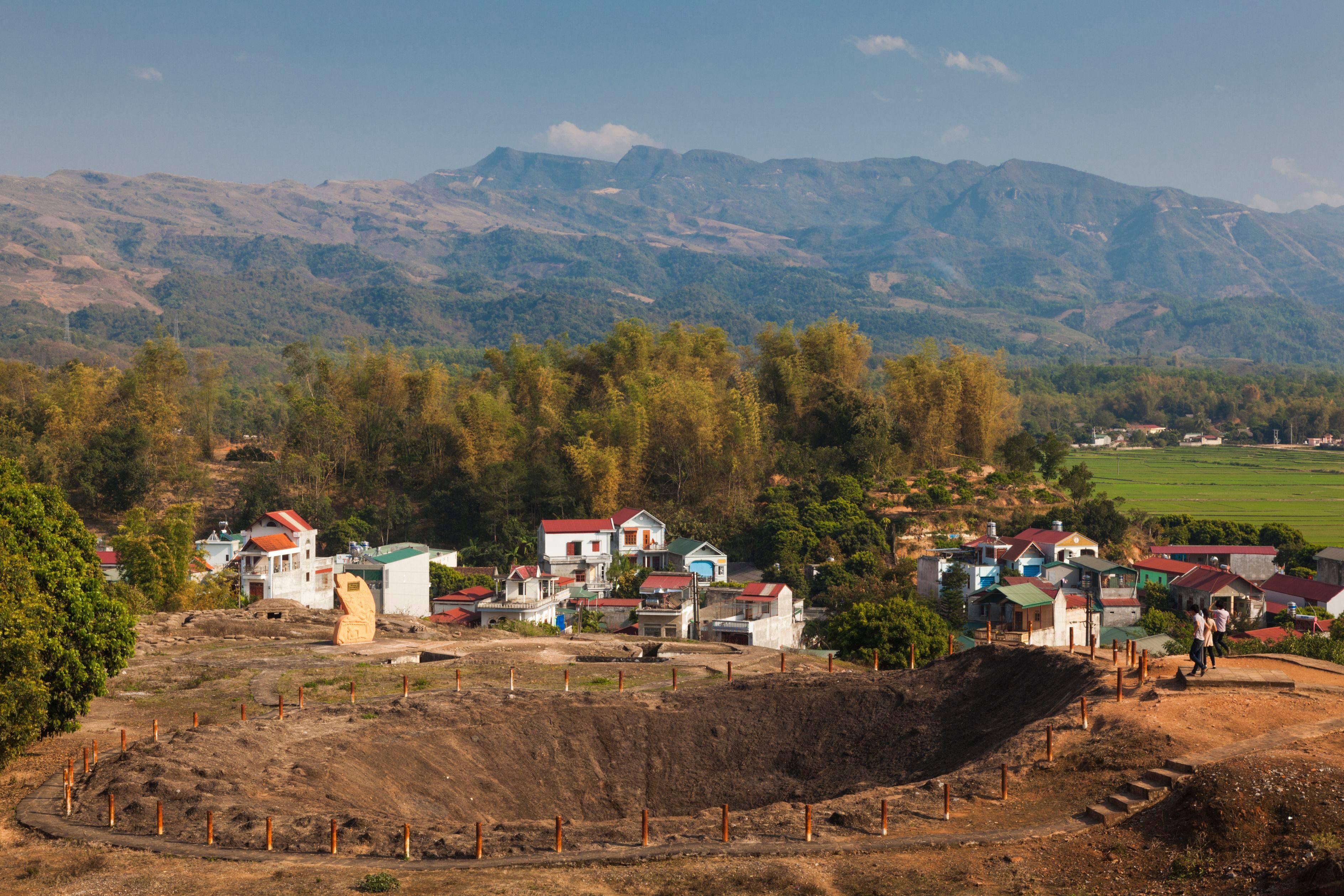A rural village with houses and a large excavation site surrounded by mountains.