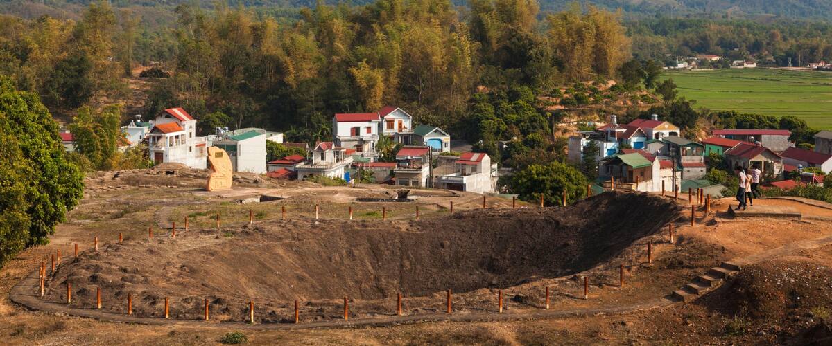 A rural village with houses and a large excavation site surrounded by mountains.