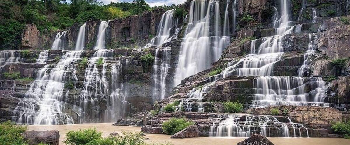 A multi-tiered waterfall with rocky terrain and lush greenery.